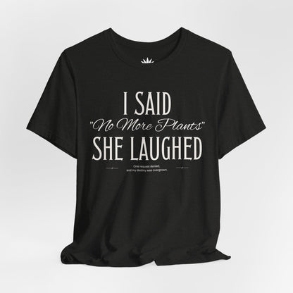 Black t-shirt with white vintage lettering that reads “I Said ‘No More Plants’ She Laughed,” a funny graphic tee for plant lovers and collectors. Hanging.